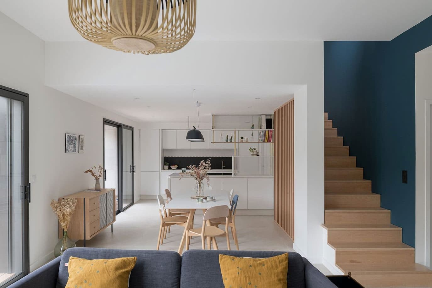 Salon ouvert sur la cuisine avec escalier bois et mur bleu, maison contemporaine