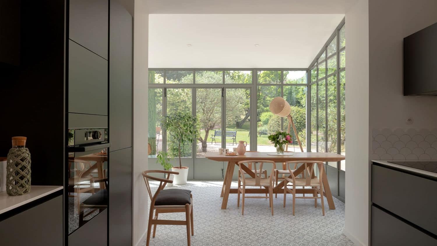 Véranda vitrée ouverte sur le jardin, table ronde et chaises en bois