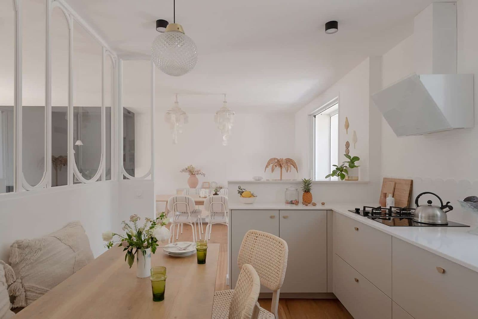 Pièce de vie ouverte sur la cuisine derrière une verrière blanche